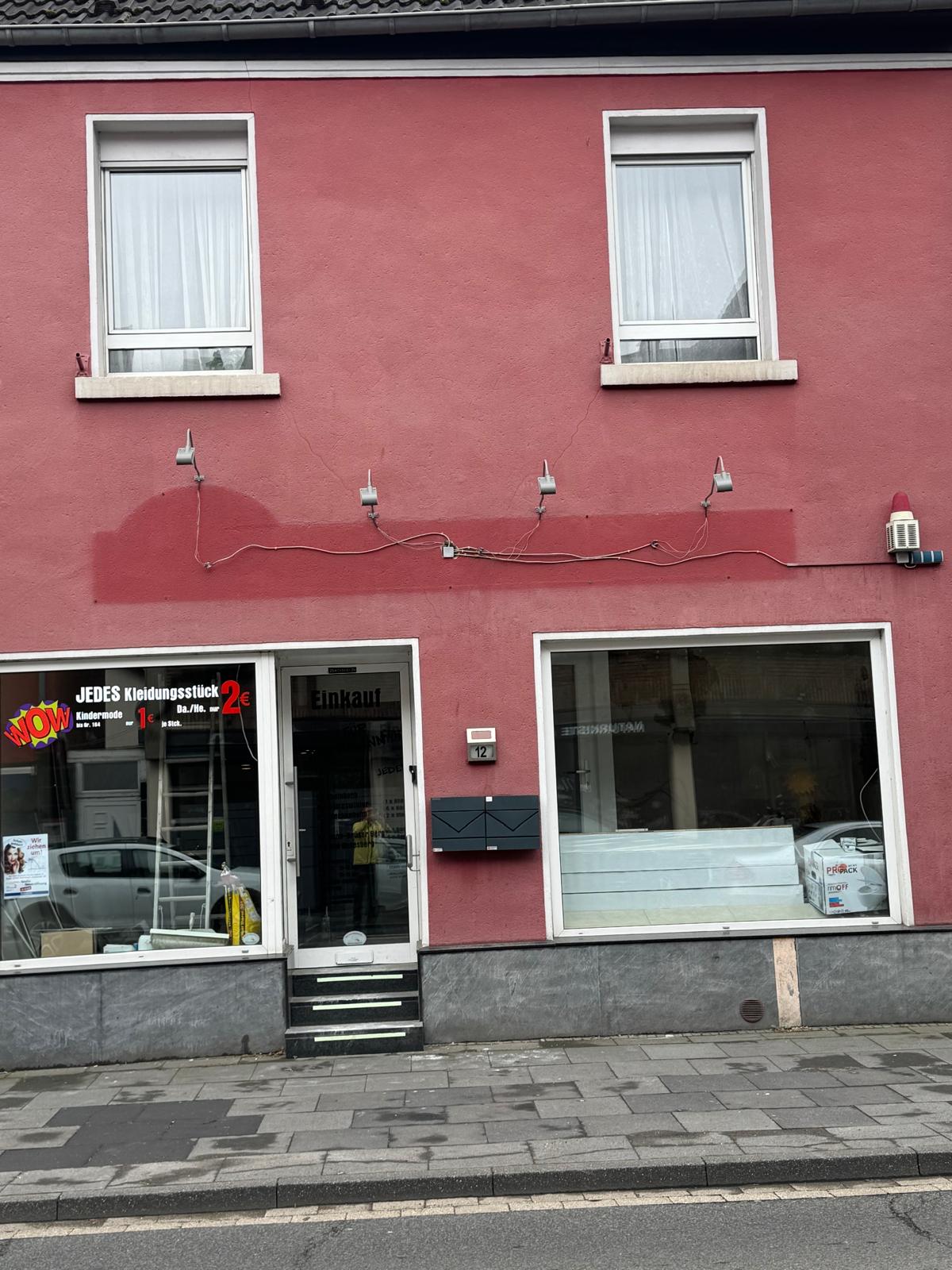 Die Hausfassade in Rheinbach vor dem Umbau, in kräftigem Rot mit zwei Schaufenstern und einer Eingangstür.